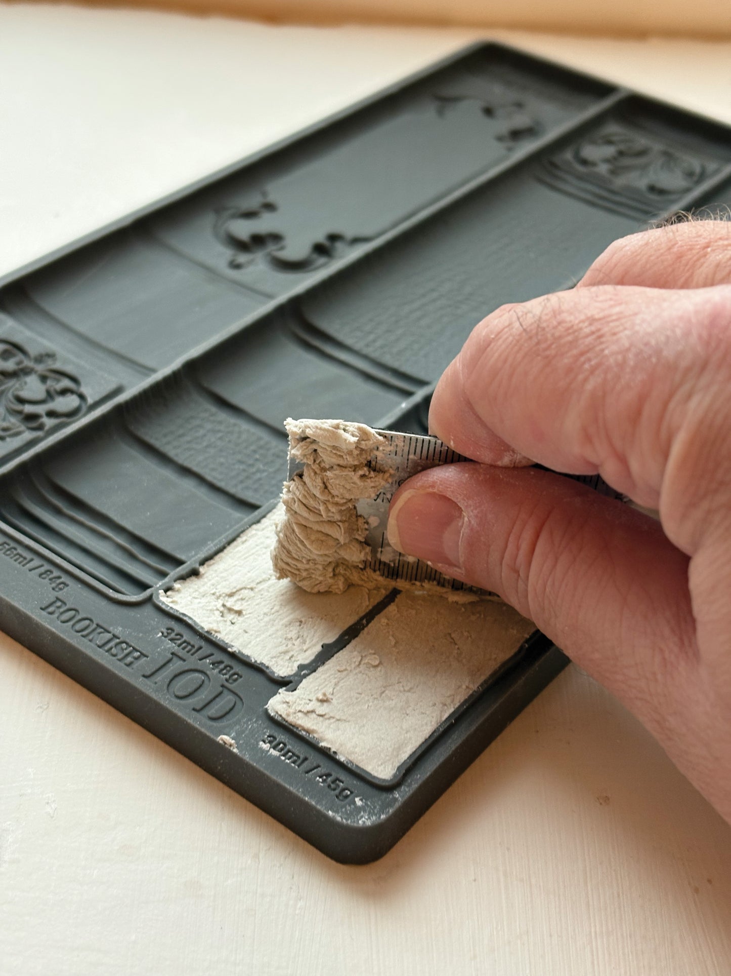 Hand using a tool to shape a small block of material on a decorative mold.