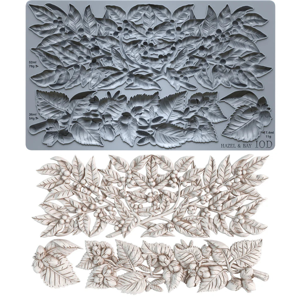 A floral leaf embossing plate made of gray metal, shown above a matching set of embossed leaf and berry cutouts in an off-white tone. Small printed markings on the plate include 'HAZEL & BAY' and '10D'.