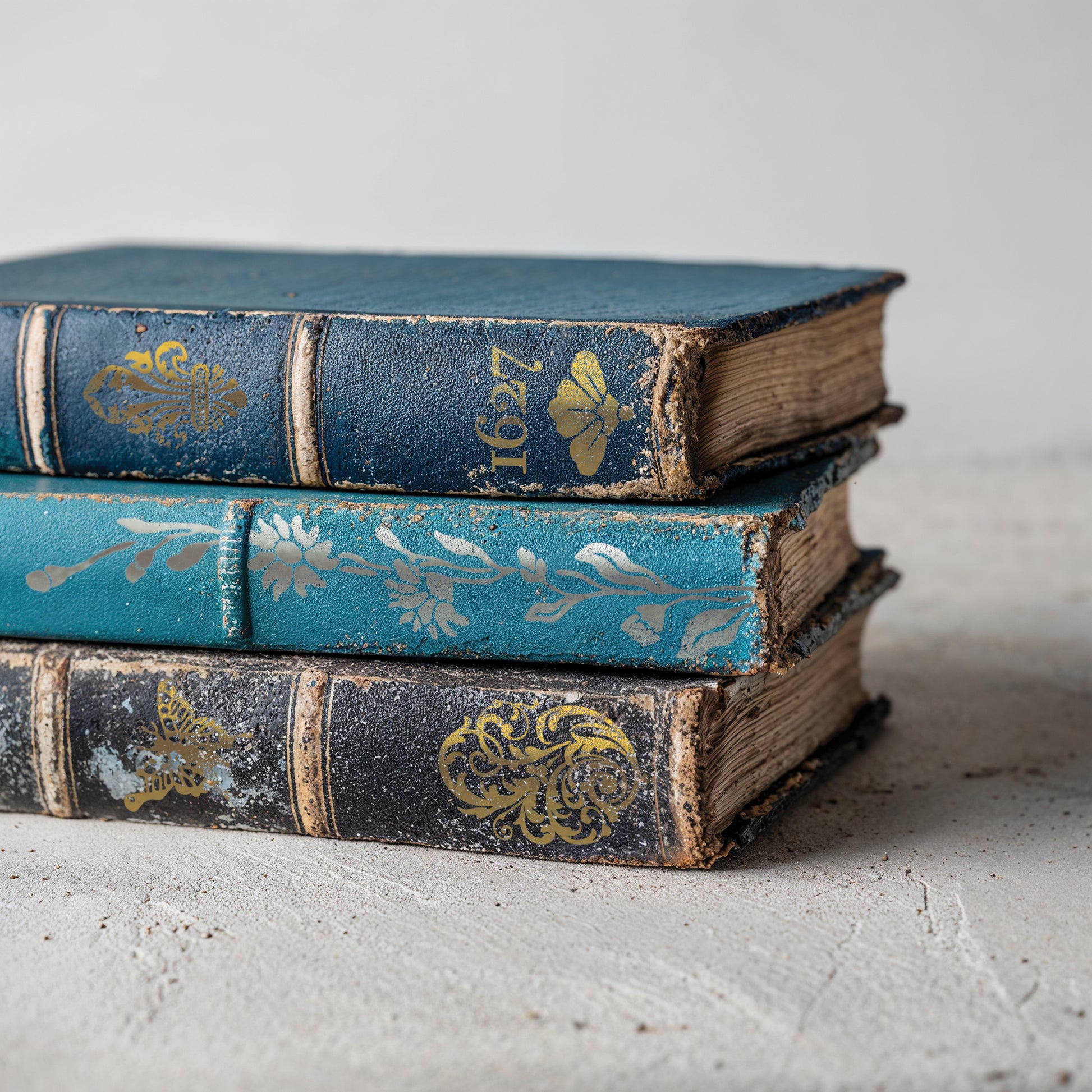 Stack of vintage books with decorative blue and gold bindings on a textured surface.