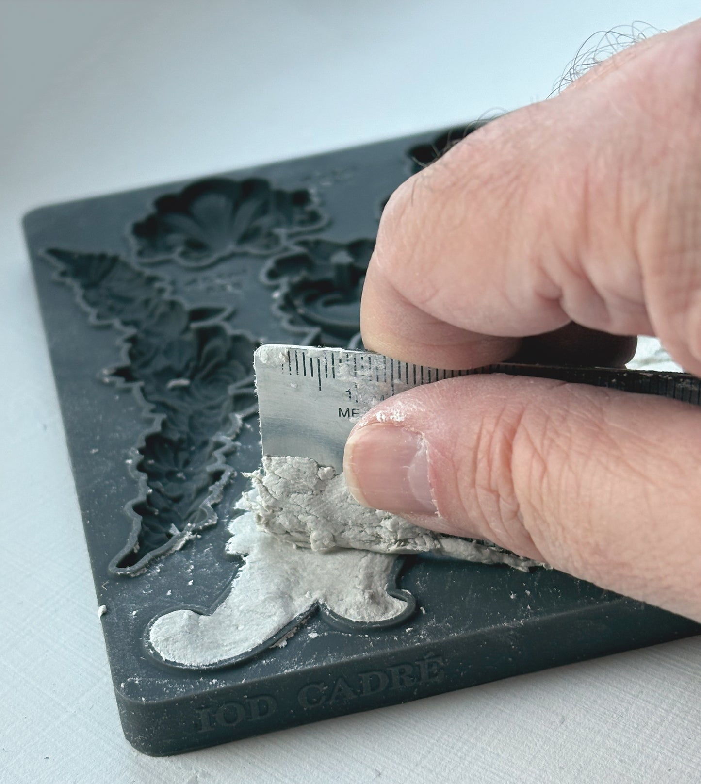 Person using a ruler to measure a decorative mold on a white surface