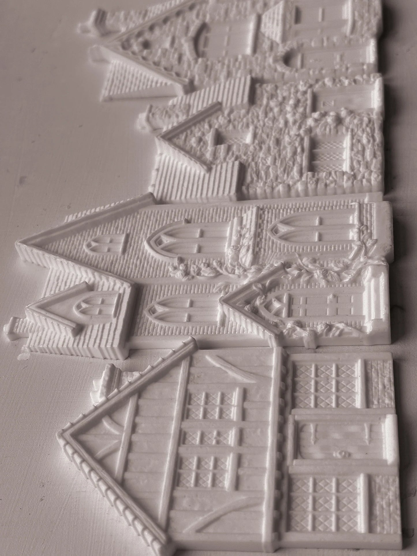 White embossed plastic or resin decorative pieces shaped like houses and cottages, shown on a plain light background.