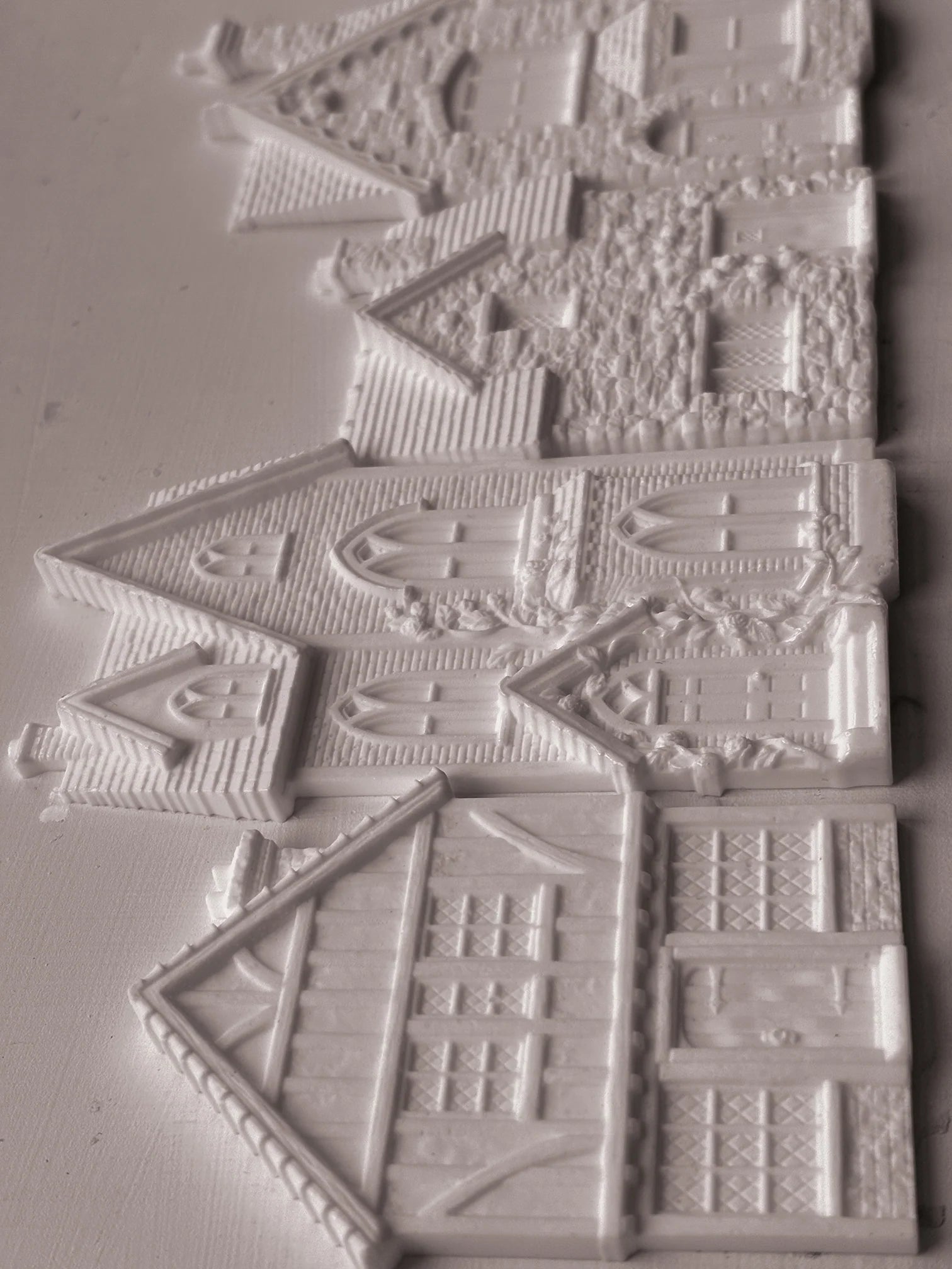 White embossed plastic or resin decorative pieces shaped like houses and cottages, shown on a plain light background.