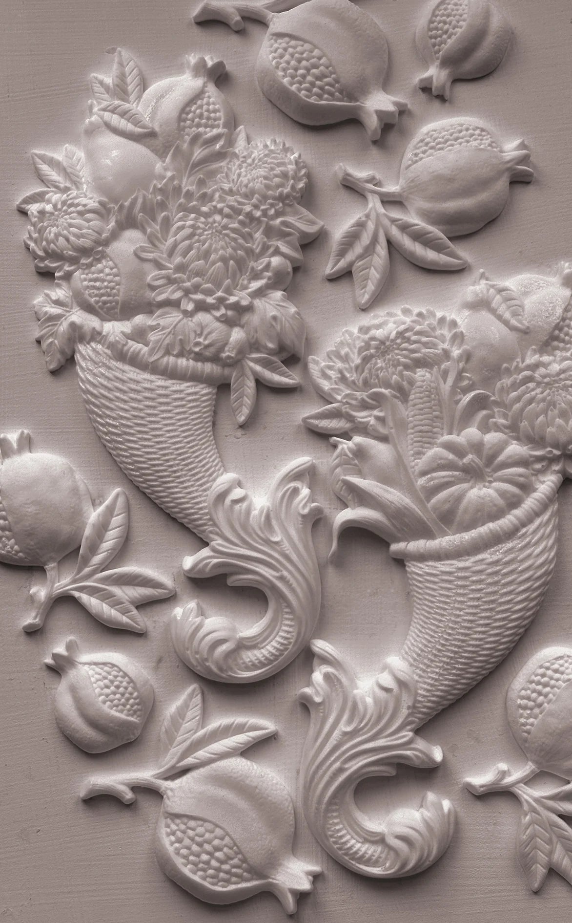 White embossed decorative wall relief featuring pomegranate motifs and floral baskets on a textured light gray surface.