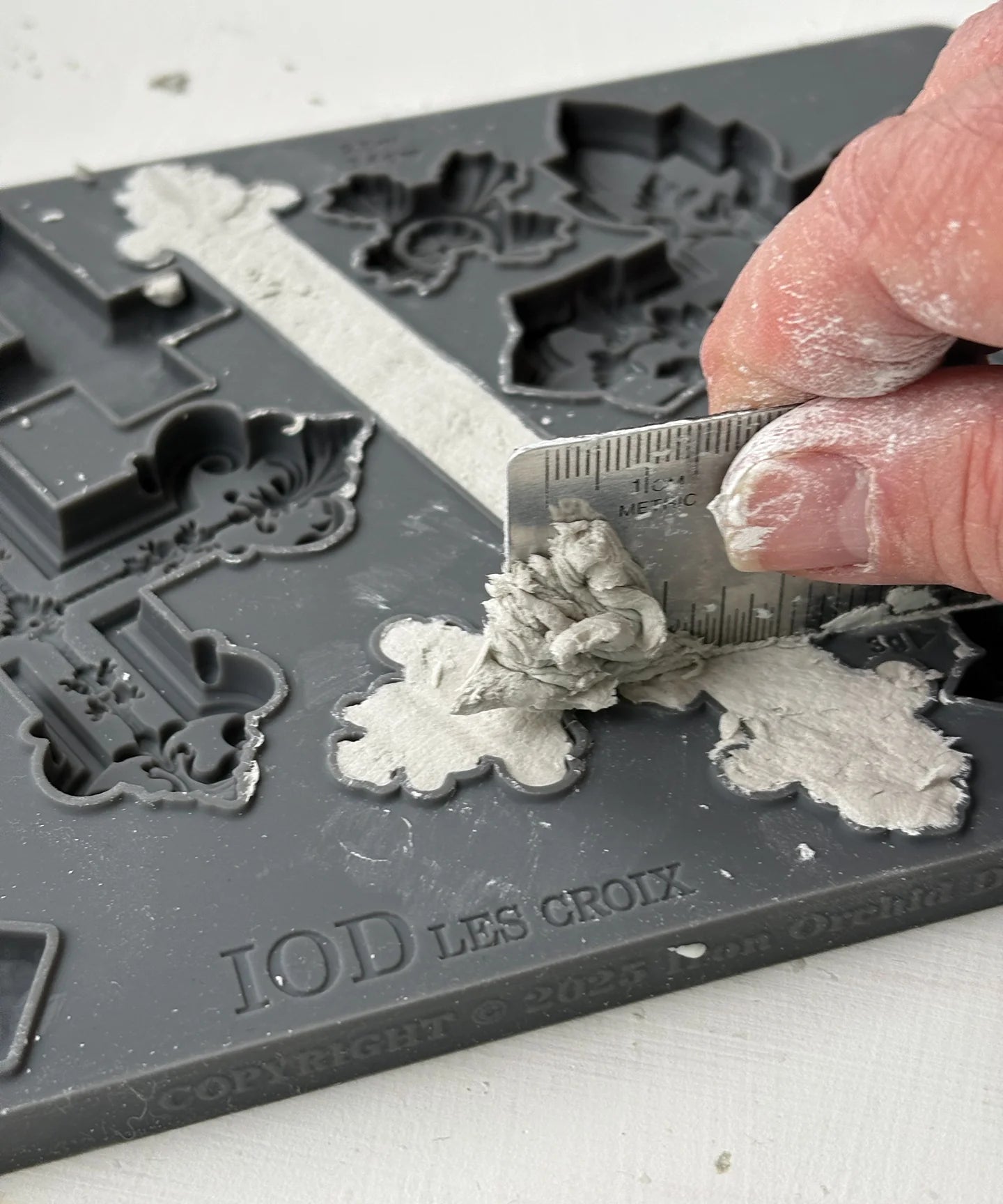 Hand using a tool to shape gray modeling material on an IOD Les Croix mold.