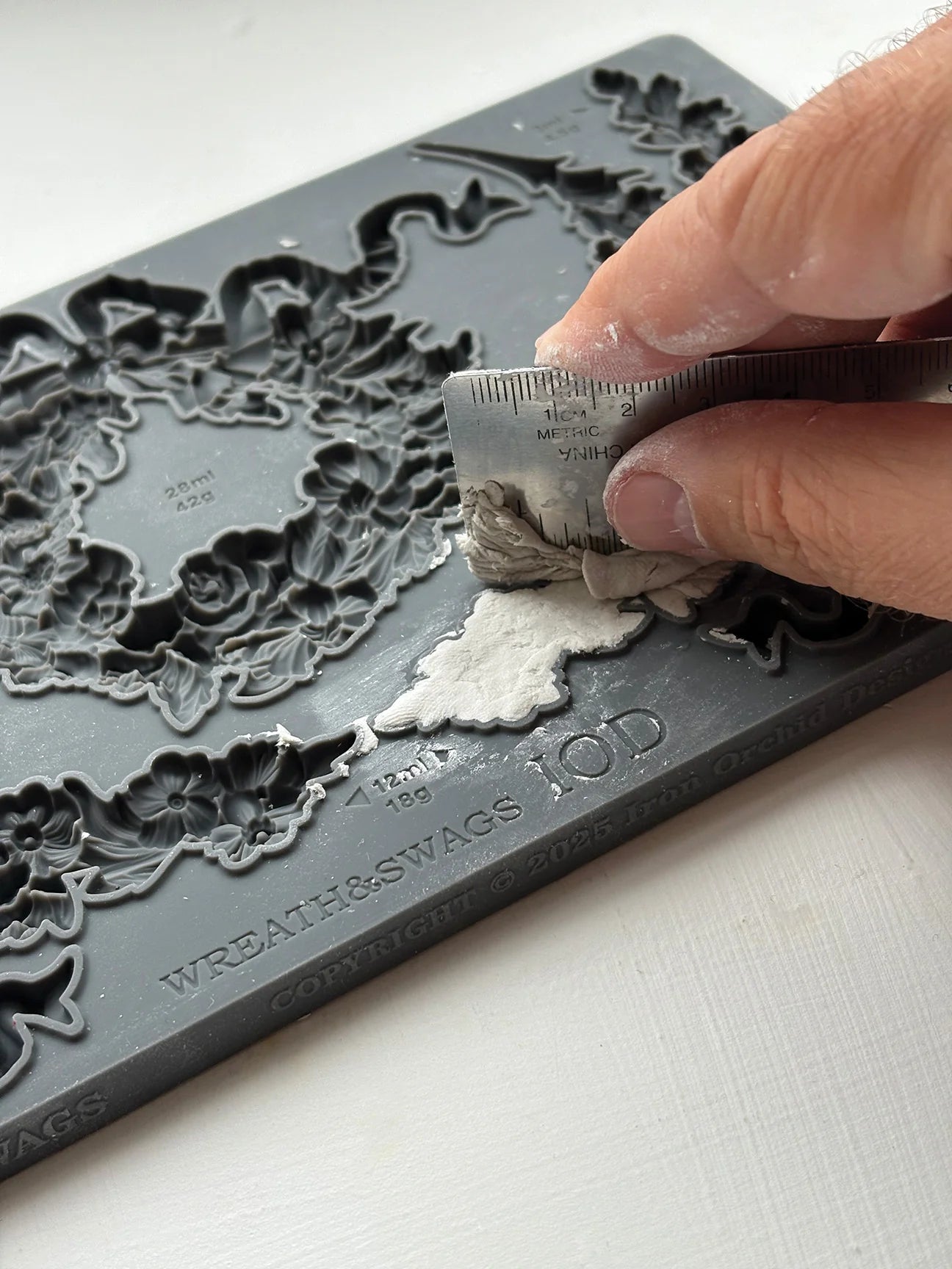 Person using a tool to carve intricate designs into a gray embossing folder.