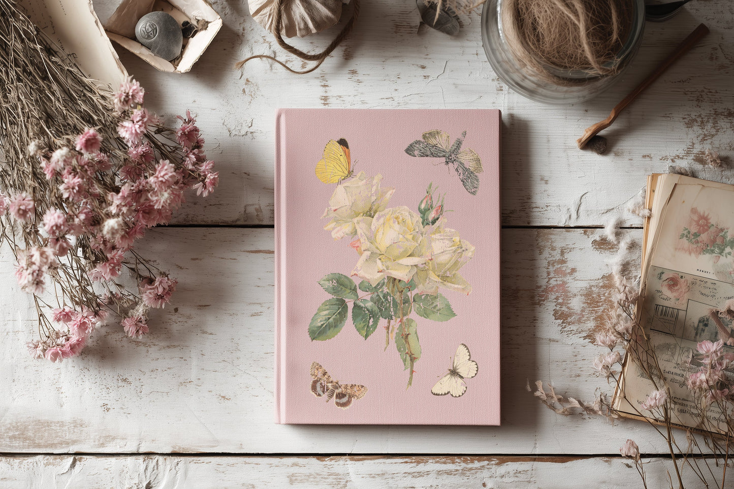 Pink notebook with floral design on a wooden surface with dried flowers and books.