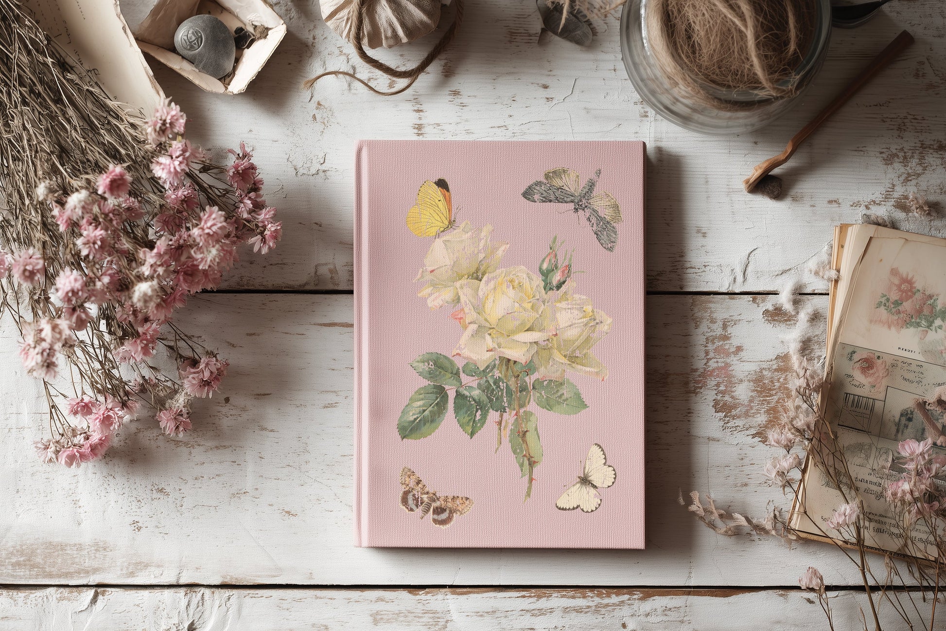 Pink notebook with floral design on a wooden surface with dried flowers and books.