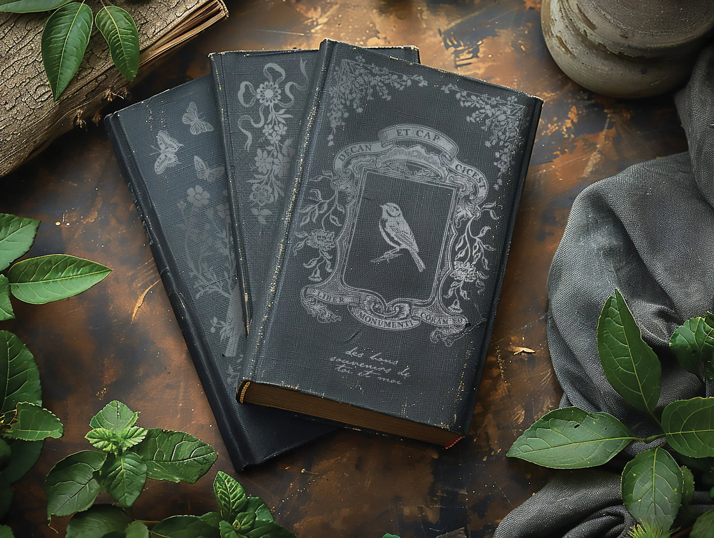 Decorative books with ornate designs on a rustic wooden surface with green leaves.