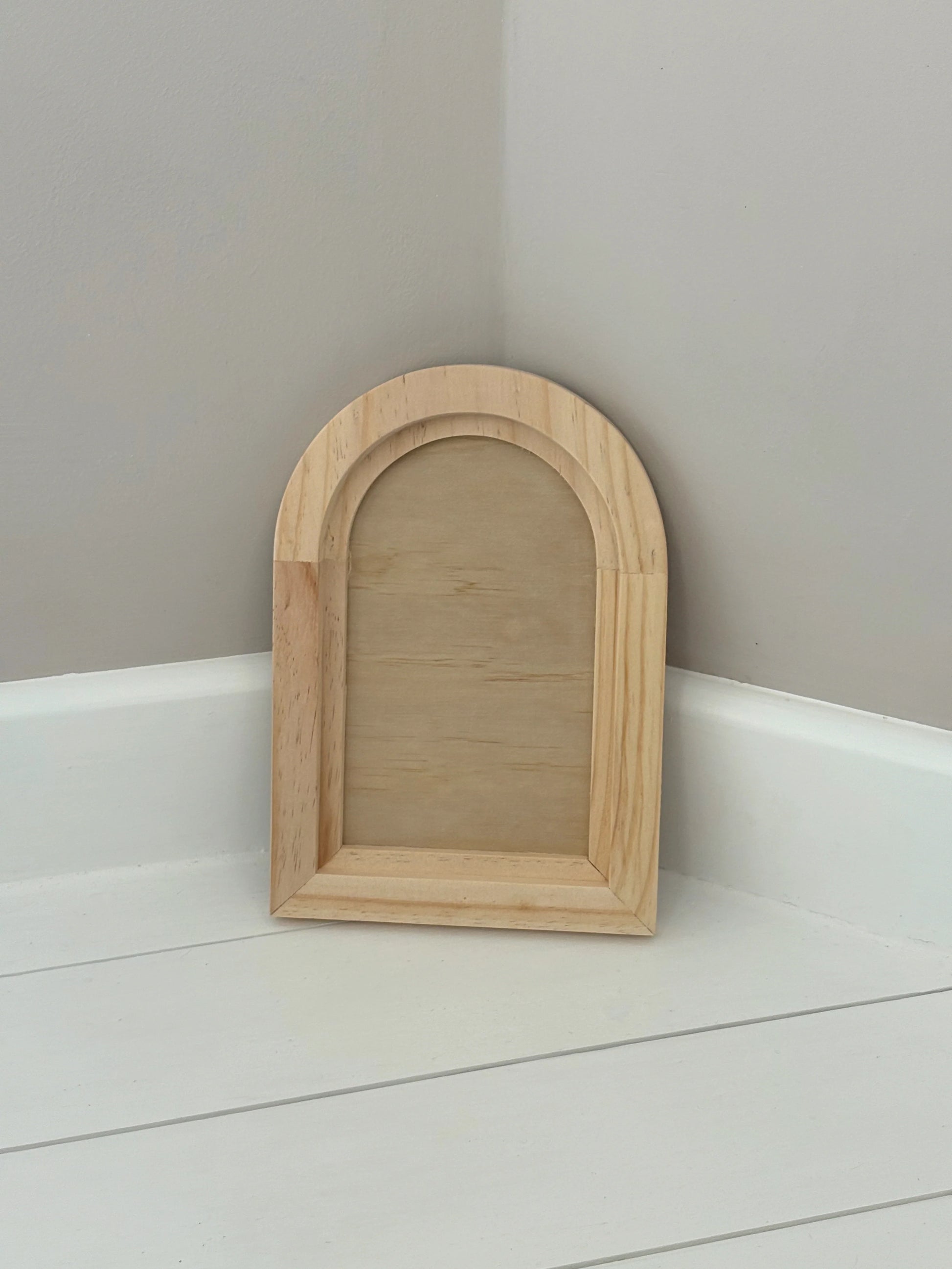 Wooden arch-shaped mirror on a white surface with a gray wall background