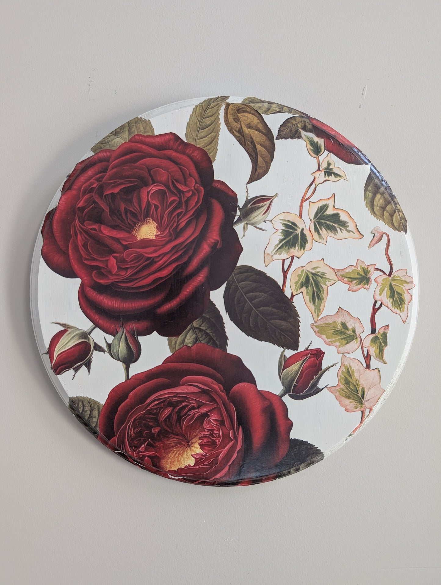 Round wood piece with red rose design on a white background