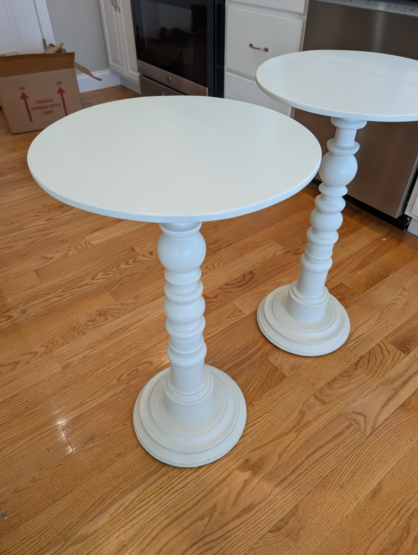 Two white pedestal tables on a wooden floor.
