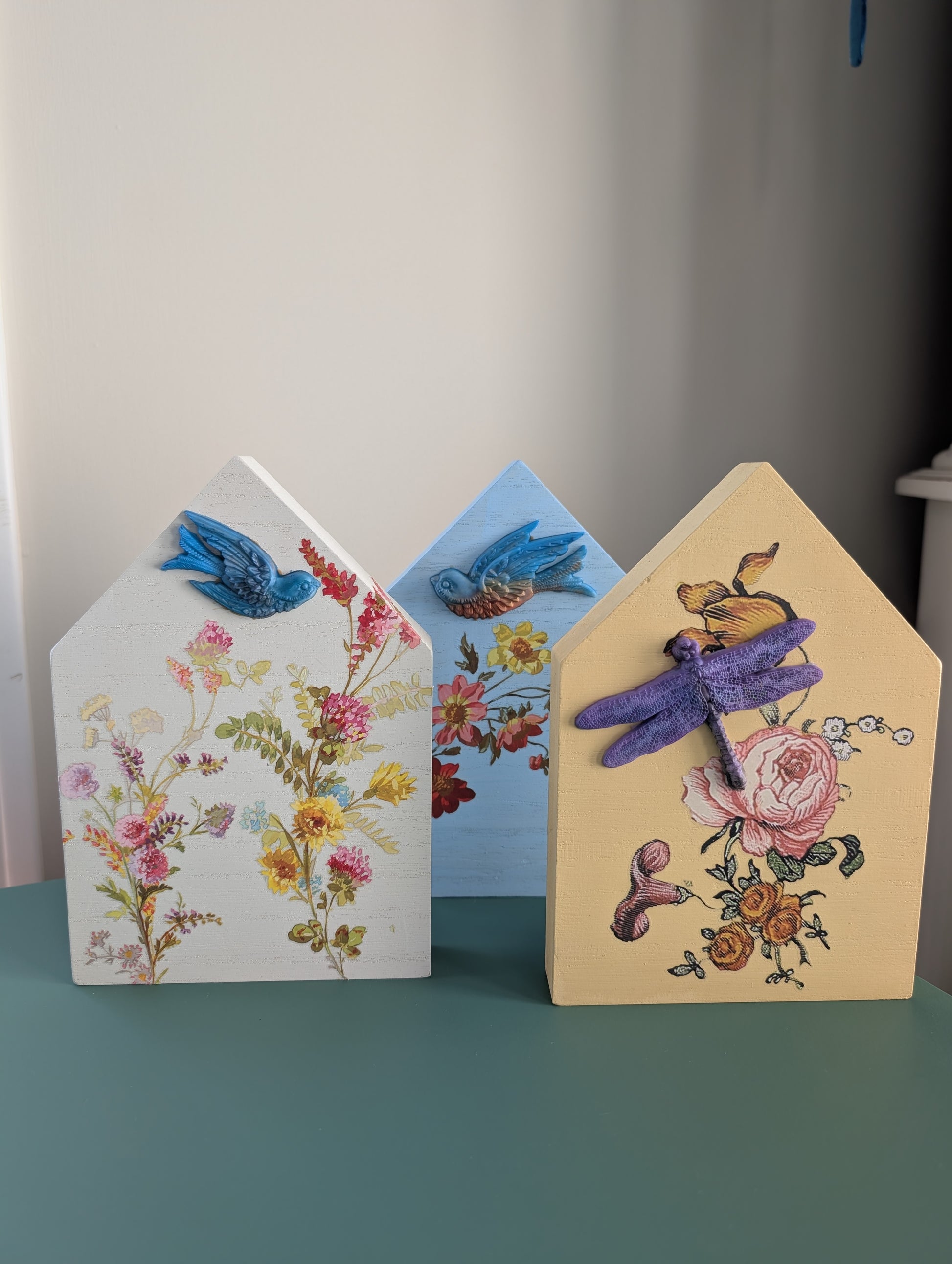 Three decorative house-shaped cards with floral and insect designs on a plain background