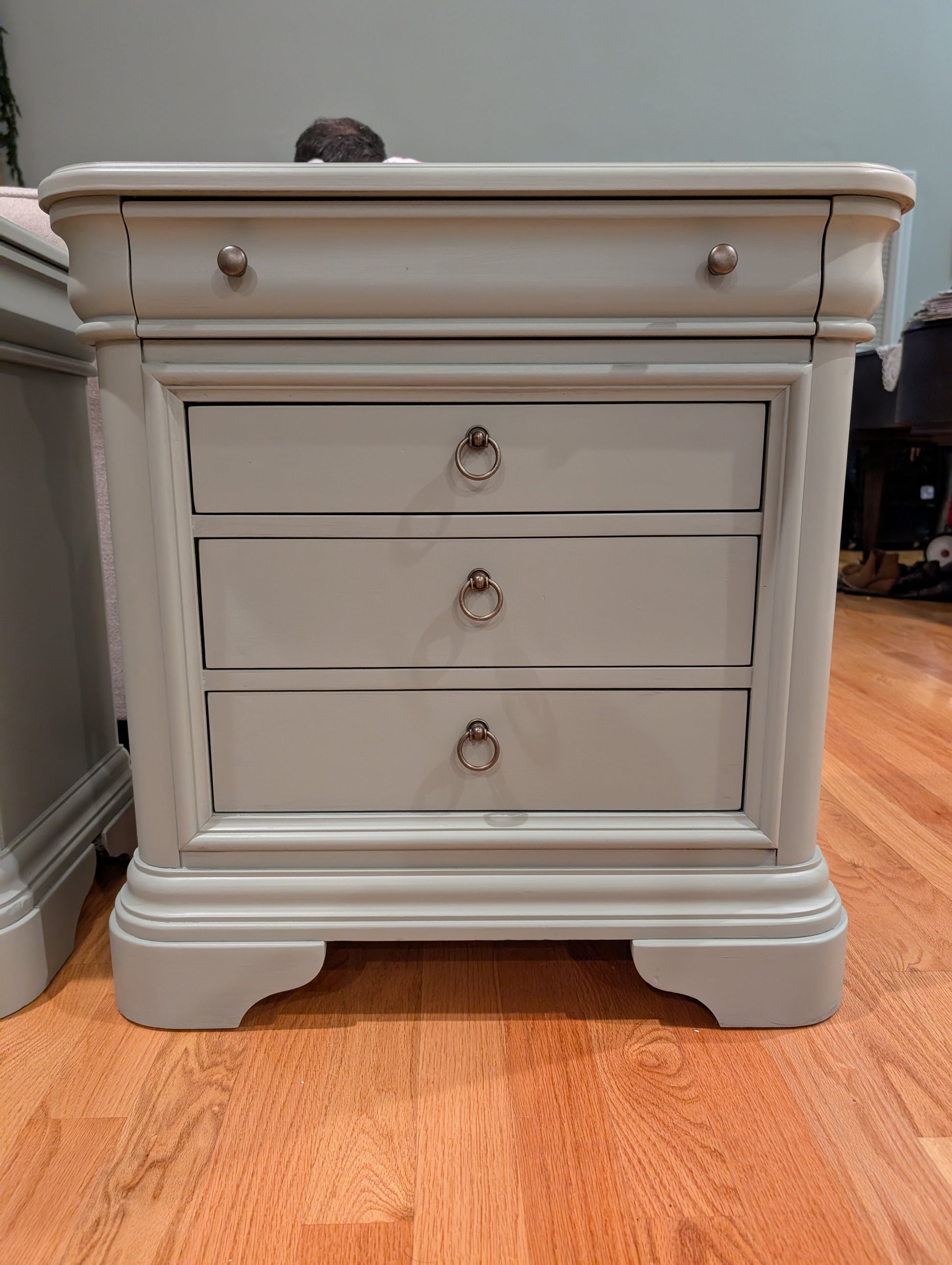 Beige nightstand with three drawers on a wooden floor.